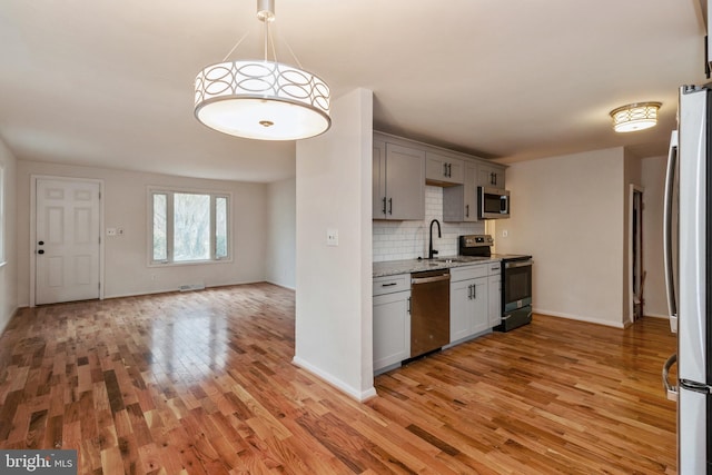 kitchen featuring sink, light hardwood / wood-style flooring, gray cabinets, appliances with stainless steel finishes, and tasteful backsplash