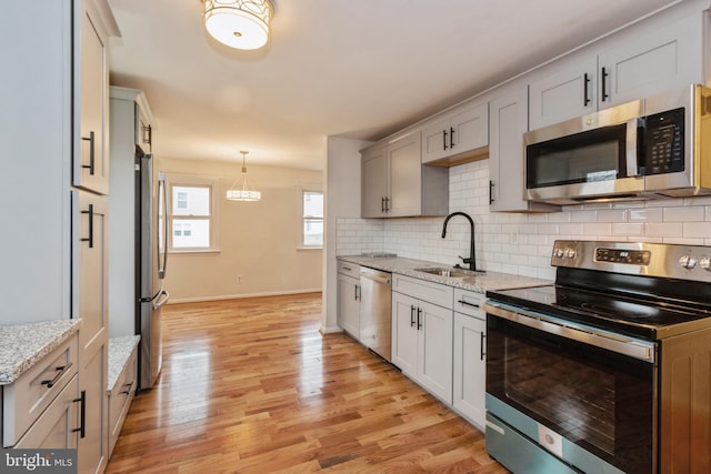 kitchen with light wood-type flooring, tasteful backsplash, light stone counters, stainless steel appliances, and sink