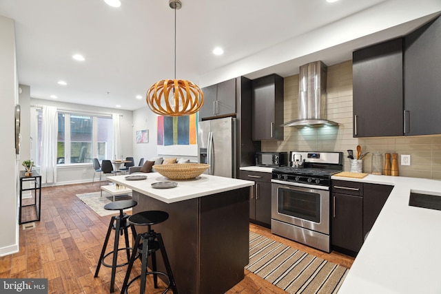 kitchen featuring appliances with stainless steel finishes, hanging light fixtures, tasteful backsplash, a kitchen breakfast bar, and wall chimney exhaust hood