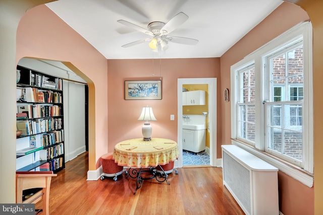 dining space featuring sink, ceiling fan, radiator heating unit, and light hardwood / wood-style flooring