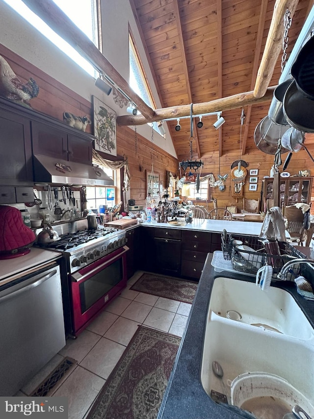 kitchen with wooden walls, lofted ceiling with beams, light tile patterned flooring, and appliances with stainless steel finishes