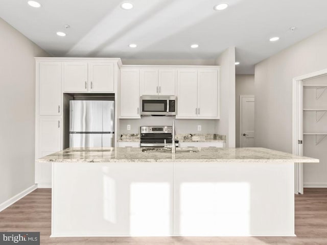 kitchen with light stone countertops, a center island with sink, appliances with stainless steel finishes, and white cabinetry