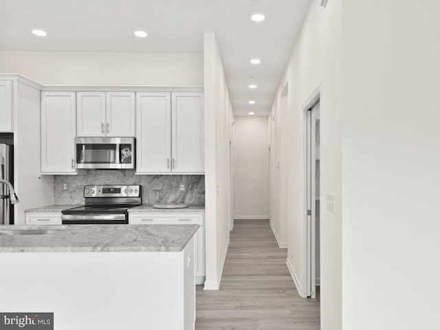 kitchen with appliances with stainless steel finishes, white cabinetry, backsplash, light stone countertops, and light hardwood / wood-style flooring