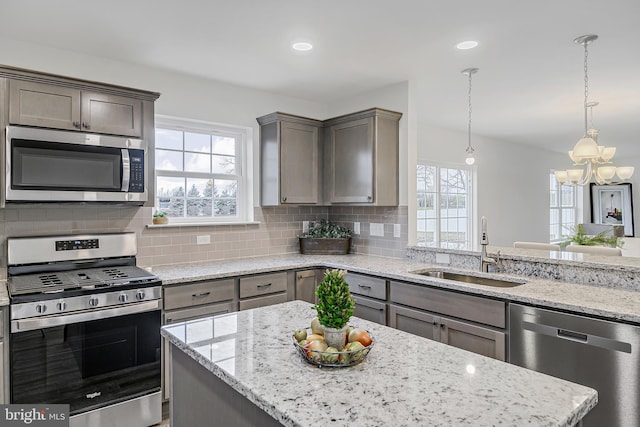 kitchen featuring stainless steel appliances, a notable chandelier, sink, and light stone countertops