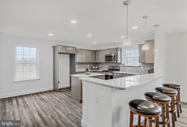 kitchen featuring pendant lighting, stainless steel appliances, a breakfast bar, backsplash, and light wood-type flooring