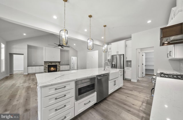 kitchen featuring light wood-type flooring, stainless steel appliances, vaulted ceiling with beams, a stone fireplace, and a center island with sink