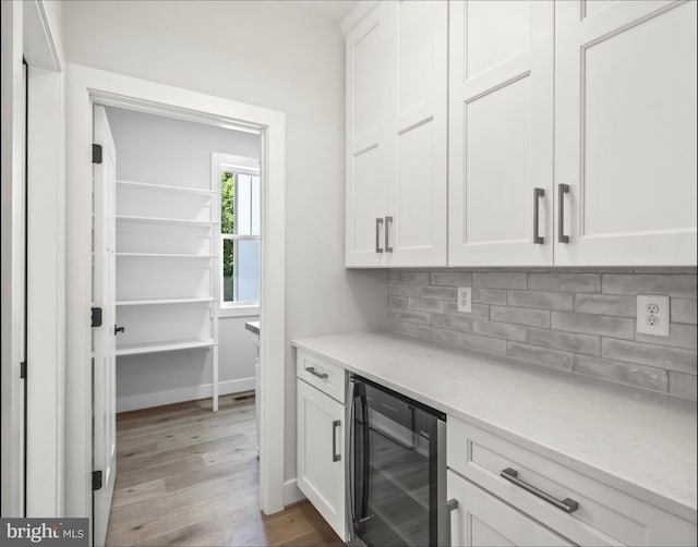 kitchen with tasteful backsplash, white cabinets, light wood-type flooring, beverage cooler, and light stone countertops