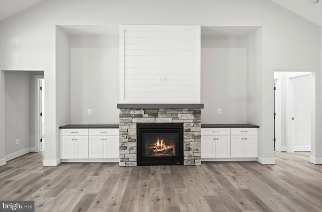 unfurnished living room with high vaulted ceiling, light wood-type flooring, and a stone fireplace