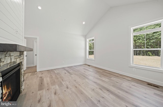 unfurnished living room featuring a stone fireplace, high vaulted ceiling, and light hardwood / wood-style flooring