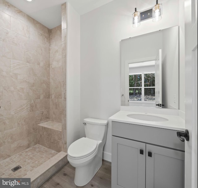 bathroom with oversized vanity, toilet, a tile shower, and hardwood / wood-style flooring