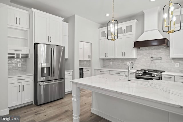 kitchen featuring stainless steel appliances, premium range hood, light hardwood / wood-style floors, white cabinetry, and light stone countertops