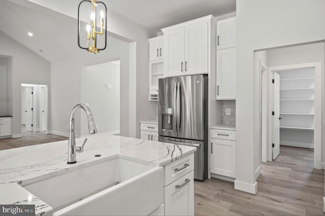 kitchen with light stone countertops, lofted ceiling, stainless steel fridge, light hardwood / wood-style floors, and white cabinets