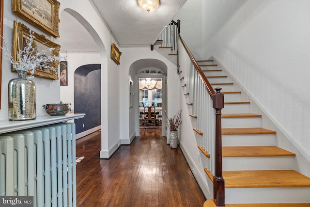 stairs with dark hardwood / wood-style floors, a notable chandelier, a textured ceiling, radiator, and ornamental molding