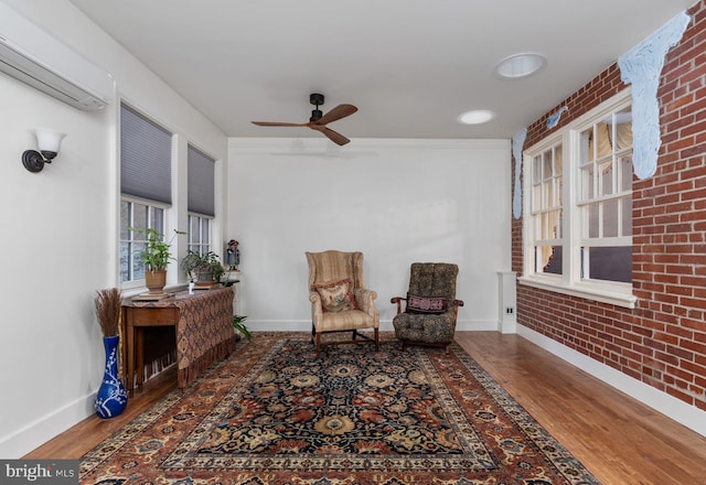 sitting room featuring a wall mounted air conditioner, dark hardwood / wood-style floors, ceiling fan, and brick wall