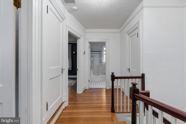 corridor with a textured ceiling and light hardwood / wood-style floors