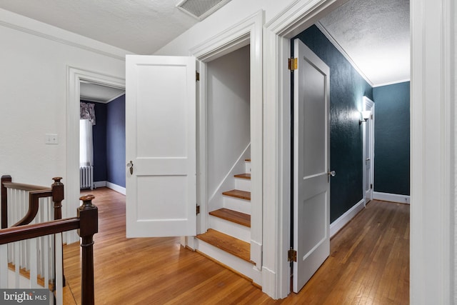 hall featuring ornamental molding, a textured ceiling, and light wood-type flooring