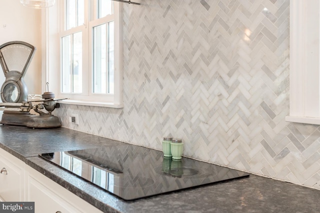 kitchen with black electric stovetop, backsplash, and white cabinetry