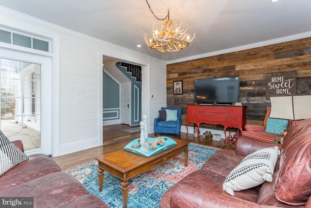 living room with wood-type flooring, ornamental molding, a notable chandelier, and wood walls