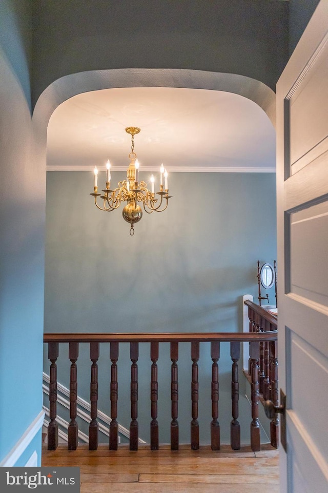 staircase featuring hardwood / wood-style flooring, crown molding, and a notable chandelier