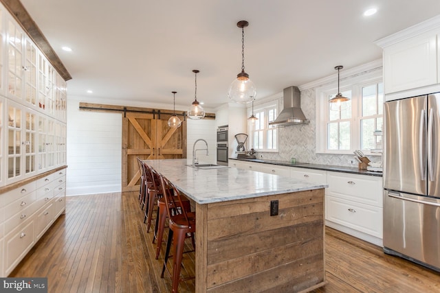 kitchen featuring dark stone counters, a spacious island, wall chimney exhaust hood, a barn door, and appliances with stainless steel finishes