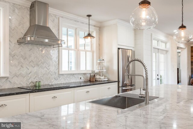 kitchen with dark stone counters, black electric stovetop, white cabinets, wall chimney exhaust hood, and stainless steel refrigerator