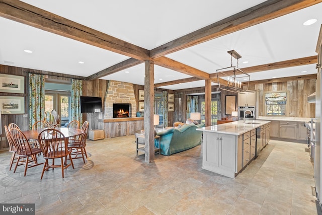 kitchen featuring decorative light fixtures, an island with sink, beam ceiling, and a wealth of natural light