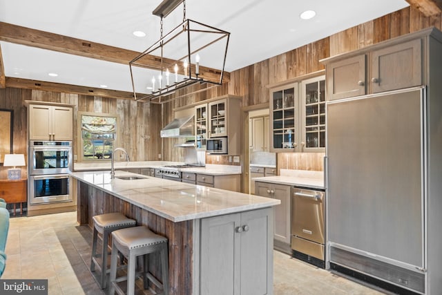 kitchen featuring appliances with stainless steel finishes, a center island with sink, wall chimney exhaust hood, sink, and light tile floors