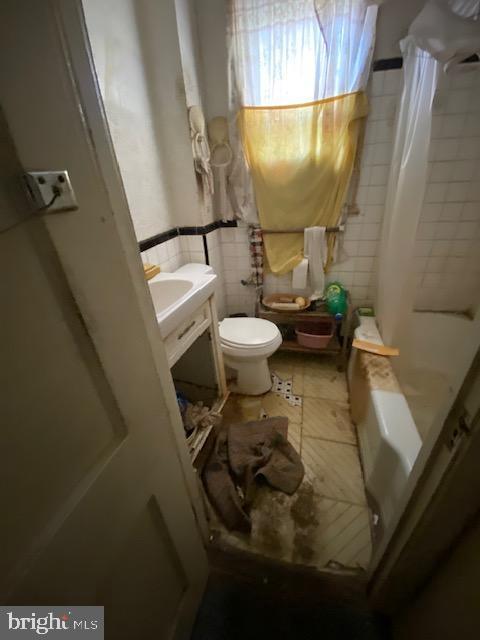 bathroom with a shower with shower curtain, toilet, and tile walls