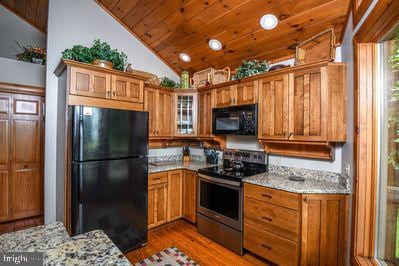 kitchen with black appliances, dark hardwood / wood-style floors, light stone counters, and vaulted ceiling