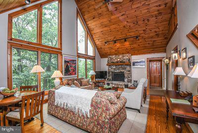 living room with high vaulted ceiling, a wealth of natural light, a stone fireplace, and wood ceiling