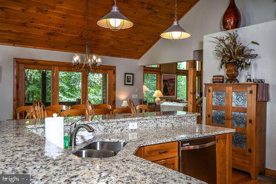 kitchen with light stone countertops, sink, hanging light fixtures, an inviting chandelier, and stainless steel dishwasher