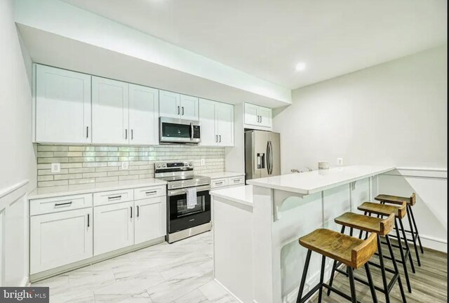 kitchen with white cabinetry, stainless steel appliances, tasteful backsplash, a kitchen breakfast bar, and kitchen peninsula