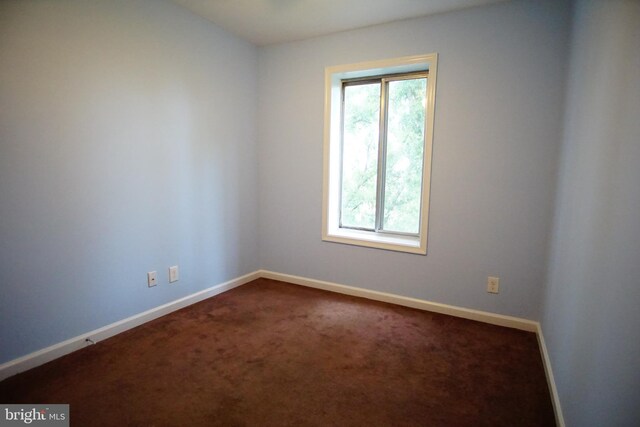 spare room with baseboards and dark carpet