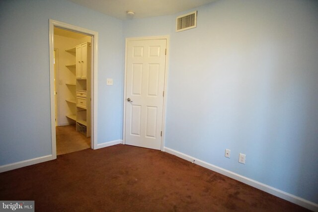unfurnished bedroom featuring baseboards, a walk in closet, dark colored carpet, and visible vents