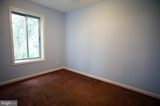 unfurnished room featuring a ceiling fan, baseboards, a wealth of natural light, and dark carpet