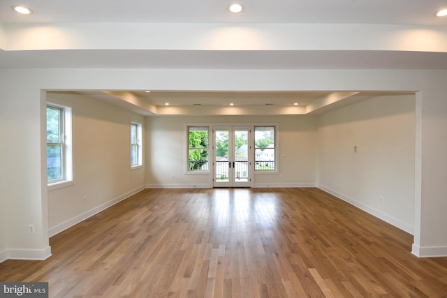 empty room featuring a tray ceiling, light hardwood / wood-style flooring, and french doors