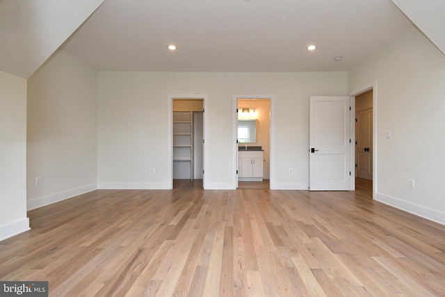 unfurnished bedroom with a walk in closet, light wood-type flooring, and connected bathroom