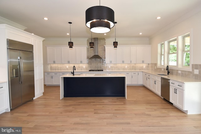 kitchen with hanging light fixtures, light hardwood / wood-style flooring, wall chimney exhaust hood, an island with sink, and stainless steel appliances