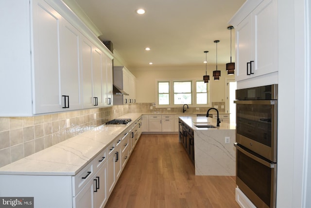 kitchen featuring light stone counters, sink, pendant lighting, light hardwood / wood-style flooring, and white cabinetry