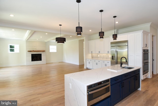 kitchen featuring pendant lighting, white cabinets, a center island with sink, sink, and appliances with stainless steel finishes