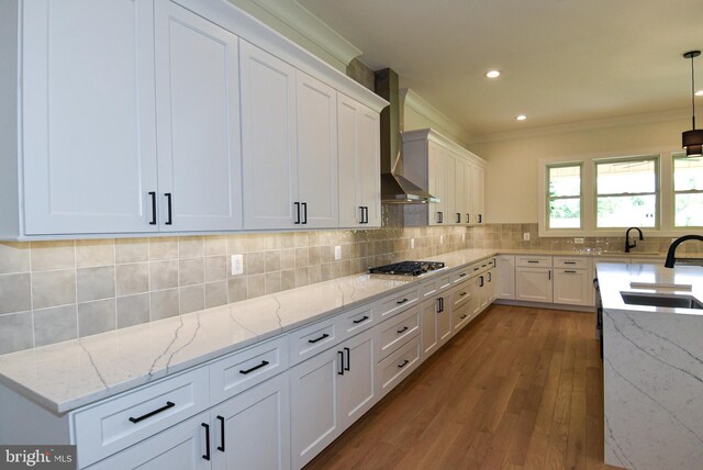 kitchen with white cabinets, hanging light fixtures, hardwood / wood-style flooring, wall chimney exhaust hood, and light stone countertops