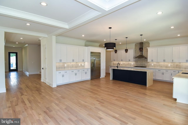 kitchen with light wood-type flooring, wall chimney exhaust hood, pendant lighting, stainless steel built in fridge, and white cabinets