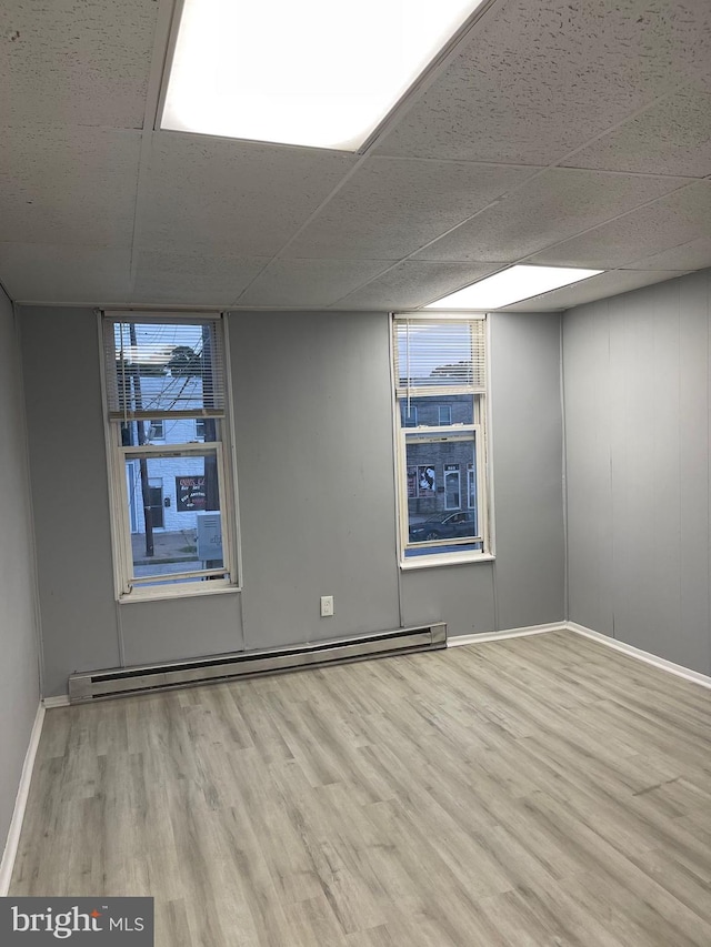 spare room with a drop ceiling, light hardwood / wood-style floors, and a baseboard heating unit