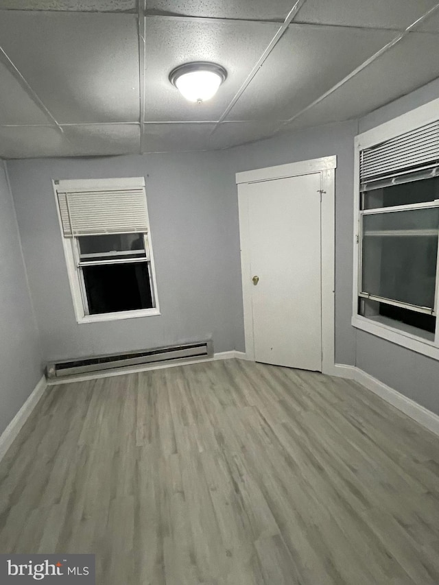 unfurnished room featuring hardwood / wood-style flooring, a paneled ceiling, and a baseboard heating unit