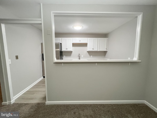 kitchen featuring white cabinetry, light hardwood / wood-style floors, stainless steel fridge, and sink