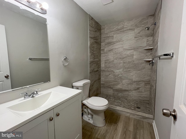 bathroom with hardwood / wood-style flooring, toilet, a tile shower, and vanity