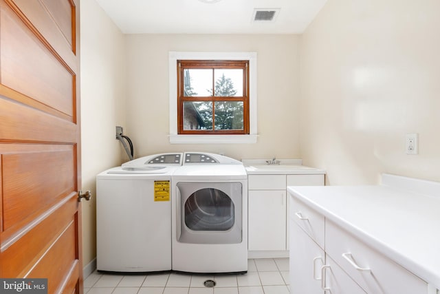 washroom with washing machine and clothes dryer, cabinets, and light tile floors