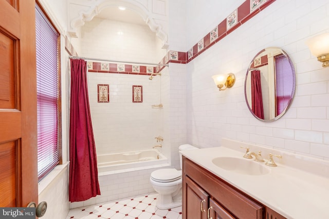 full bathroom with tile walls, tile floors, toilet, vanity with extensive cabinet space, and shower / bath combo with shower curtain