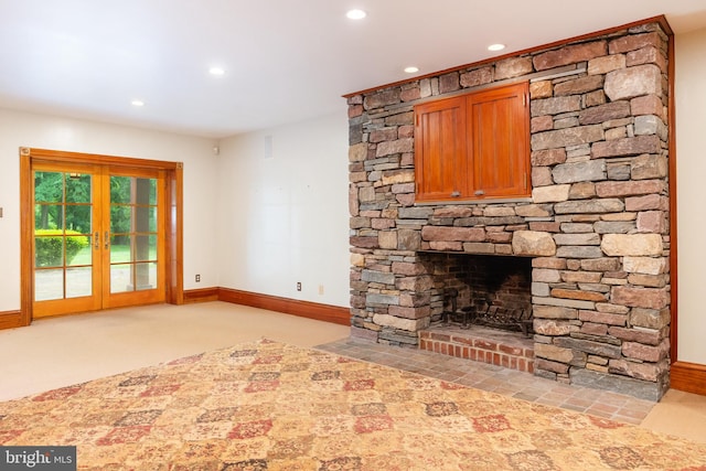 unfurnished living room featuring light carpet, a stone fireplace, and french doors