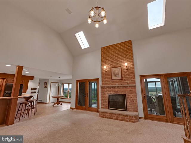 carpeted living room featuring a brick fireplace, brick wall, high vaulted ceiling, a skylight, and a chandelier